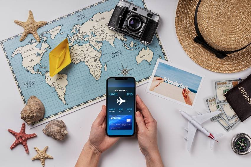 Person booking air ticket on phone with world map, camera, passport, and travel planning essentials showing how Travel Tweaks Offers work.